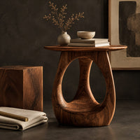 Corner detail of round side table with an open teardrop pedestal and a flared foot beside wood, brass and linen samples