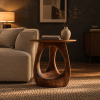 Round side table with an open teardrop pedestal and a flared foot in a dark living room at golden hour