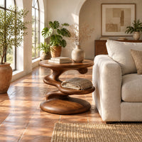 Circular side table with a spiral stem, middle shelf disc and wide base in a bright living room with arched windows and plants