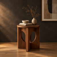 Round side table with a panel base and tall oval cutouts in a dark studio against a charcoal plaster wall