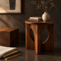 Corner detail of round side table with a panel base and tall oval cutouts beside wood, brass and linen samples