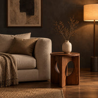 Round side table with a panel base and tall oval cutouts in a dark living room at golden hour