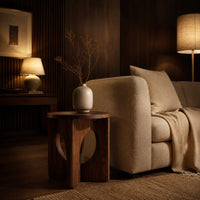 Round side table with a panel base and tall oval cutouts in an evening living room with walnut wall paneling