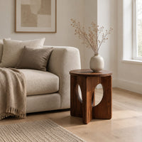 Round side table with a panel base and tall oval cutouts in a Scandinavian living room with white walls
