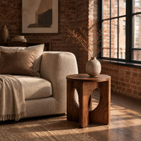 Round side table with a panel base and tall oval cutouts in an industrial loft living room with exposed brick