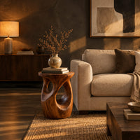Round side table with a vase shaped base and twisting cutouts in a dark living room at golden hour