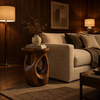 Round side table with a vase shaped base and twisting cutouts in an evening living room with walnut wall paneling