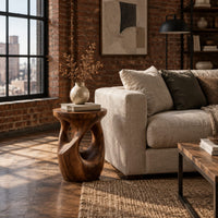 Round side table with a vase shaped base and twisting cutouts in an industrial loft living room with exposed brick