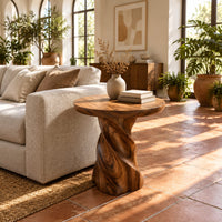 Side table with a circular top on a twisted spiral pedestal in a bright living room with arched windows and plants