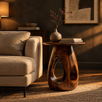 Round side table with teardrop cutouts in a pear shaped pedestal in a dark living room at golden hour