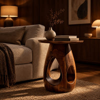 Round side table with teardrop cutouts in a pear shaped pedestal in an evening living room with walnut wall paneling