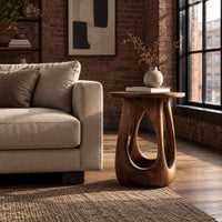 Side table with a round wood top and a bulging base with teardrop cutouts in an industrial loft living room with exposed brick