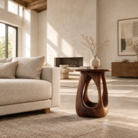 Side table with a round wood top and a bulging base with teardrop cutouts in a bright open plan living room