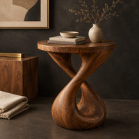 Corner detail of side table with a circular top and a twisted figure eight pedestal base beside wood, brass and linen samples