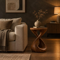 Side table with a circular top and a twisted figure eight pedestal base in a dark living room at golden hour