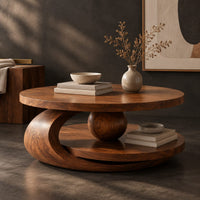 Corner detail of round two tier coffee table with a wooden sphere and crescent shaped support beside wood, brass and linen samples