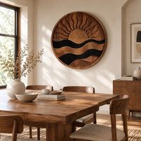 Circular carved sun and wave wall art with dark and natural wood bands beside a dining table in natural light