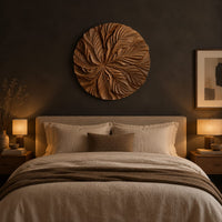 Circular wood disc carved with overlapping leaves that radiate from the center above a bed in a dusk lit bedroom