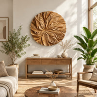 Circular wood disc carved with overlapping leaves that radiate from the center in a bright sunroom with green plants