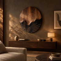 Circular wood wall art with smooth grain above dark carved wave ridges above a low console in an evening living room