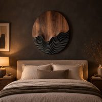 Circular wood wall art with smooth grain above dark carved wave ridges above a bed in a dusk lit bedroom