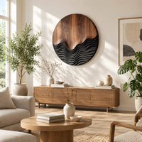 Circular wood wall art with smooth grain above dark carved wave ridges in a bright sunroom with green plants