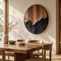 Circular wood wall art with smooth grain above dark carved wave ridges beside a dining table in natural light