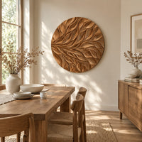 Circular wall art panel carved with sweeping layered leaves beside a dining table in natural light