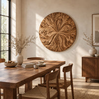Round wood wall art with swirling carved petals in relief beside a dining table in natural light