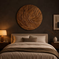 Round wooden wall relief with swirling carved ridges above a bed in a dusk lit bedroom