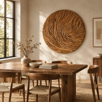 Round wooden wall relief with swirling carved ridges beside a dining table in natural light