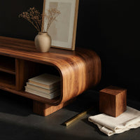 Corner detail of rounded TV console with three open bays beside wood, brass and linen samples