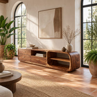 Low rounded tv stand with three drawers and open shelves in a bright living room with arched windows and plants