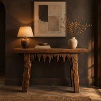 Rustic plank console table with thick legs and a jagged drip edge apron in a dark entryway at golden hour