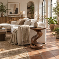 Side table with a twisting pedestal and a coiled loop base in a bright living room with arched windows and plants