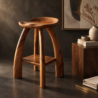 Corner detail of saddle seat bar stool with curved legs and a low square shelf beside wood, brass and linen samples