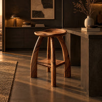 Saddle seat bar stool with curved legs and a low square shelf in a dark kitchen at golden hour