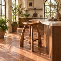 Saddle seat bar stool with curved legs and a low square shelf in a bright kitchen with arched windows and plants