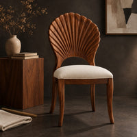 Corner detail of dining chair with a carved fan shaped back and cushioned seat beside wood, brass and linen samples