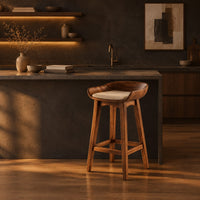 Bar stool with a scooped wooden seat and a cream cushion in a dark kitchen at golden hour