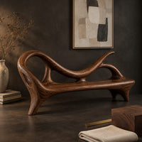 Corner detail of bench with a looping scroll back and a flat seat on splayed legs beside wood, brass and linen samples