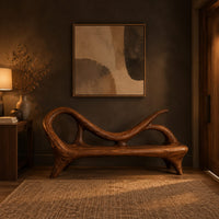 Bench with a looping scroll back and a flat seat on splayed legs in a dark entryway at golden hour