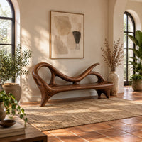 Bench with a looping scroll back and a flat seat on splayed legs in a bright entryway with arched windows and plants