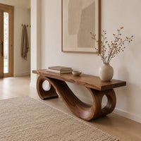 Wooden bench with a thick plank seat on a flowing scroll shaped base in a Scandinavian entryway with white walls