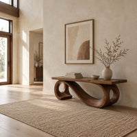 Wooden bench with a thick plank seat on a flowing scroll shaped base in a bright open plan entryway