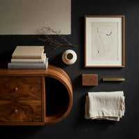 Corner detail of scroll shelf TV stand with a cantilevered top beside wood, brass and linen samples