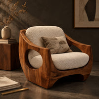 Corner detail of low accent chair with a sculpted wood shell and circular side openings beside wood, brass and linen samples