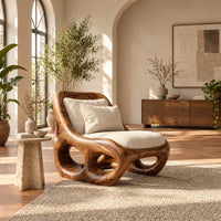Sculpted wood accent chair with open loops in the base and loose cushions in a bright living room with arched windows and plants