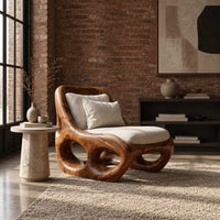 Sculpted wood accent chair with open loops in the base and loose cushions in an industrial loft living room with exposed brick