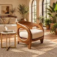 Barrel shaped chair with open oval cutouts and a cream seat cushion in a bright living room with arched windows and plants